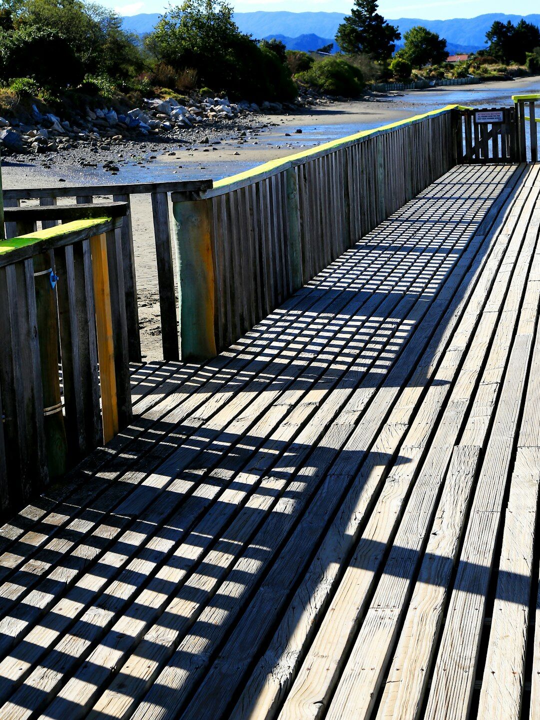Wooden bridge over a calm river estuary surrounded by dunes and pine trees